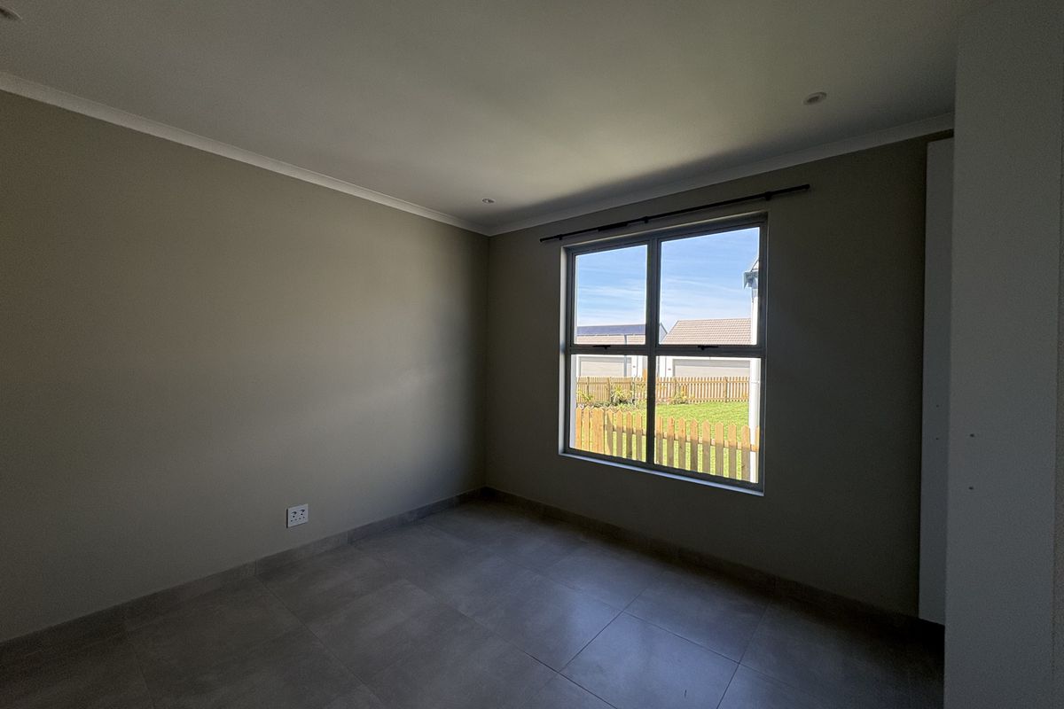 A clean, empty bedroom featuring neutral wall paint, large window with natural light, tiled flooring, and a built-in cupboard.