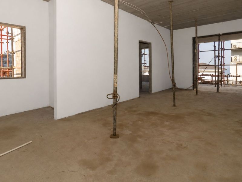 An unfinished open-plan interior space currently under construction, featuring exposed concrete ceilings, concrete flooring, and temporary structural support props.