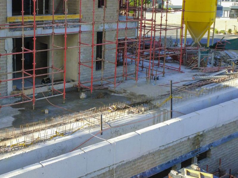 An elevated view of an apartment building currently under construction, featuring exposed concrete blockwork, scaffolding, and ongoing structural work.
