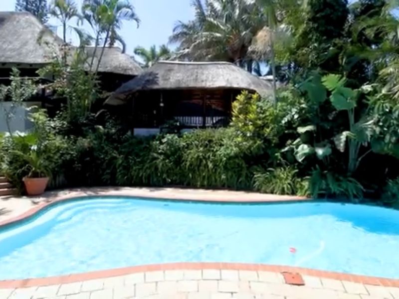 A private swimming pool area featuring brick paving, stone steps, and a thatched roof outdoor structure surrounded by lush tropical landscaping.