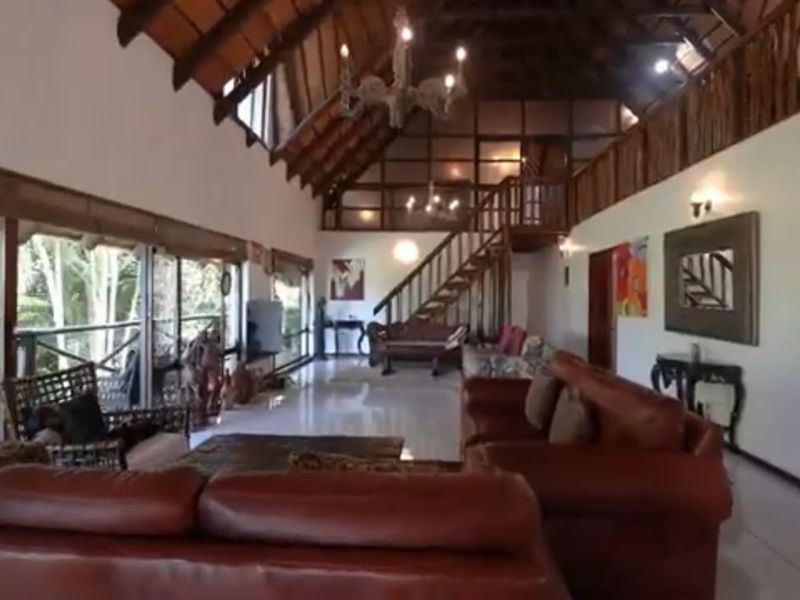 Spacious living area featuring a high vaulted timber ceiling, mezzanine level with staircase, and large sliding glass doors opening to the exterior.