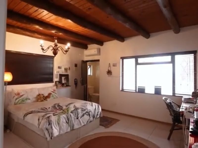 A bedroom featuring exposed timber ceiling beams, tiled flooring, and an en-suite bathroom, offering a rustic aesthetic with integrated climate control.