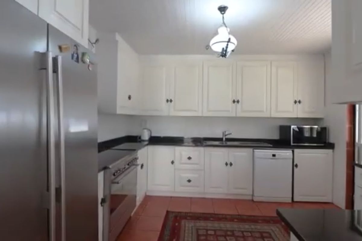 A functional kitchen featuring white cabinetry, dark granite countertops, stainless steel appliances, and terracotta-style floor tiles.