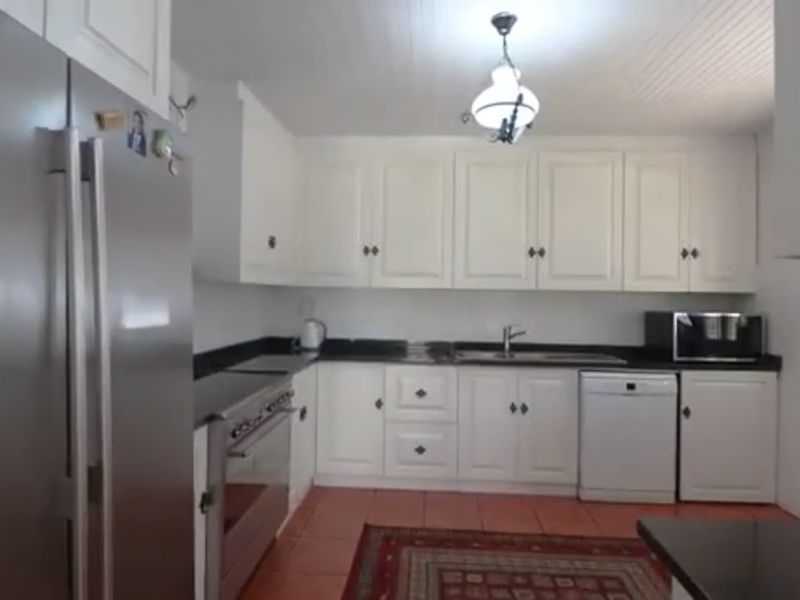 A functional kitchen featuring white cabinetry, dark granite countertops, stainless steel appliances, and terracotta-style floor tiles.