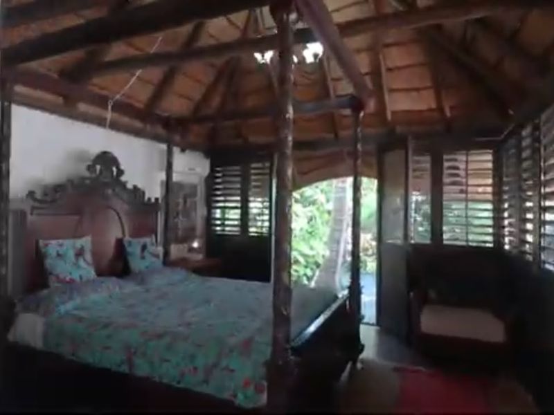 A unique bedroom featuring a high thatched ceiling with exposed timber rafters and traditional timber louvered shutters providing natural light and ventilation.