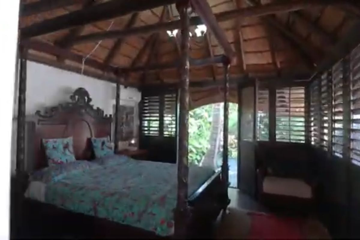 A unique bedroom featuring a high thatched ceiling with exposed timber rafters and traditional timber louvered shutters providing natural light and ventilation.