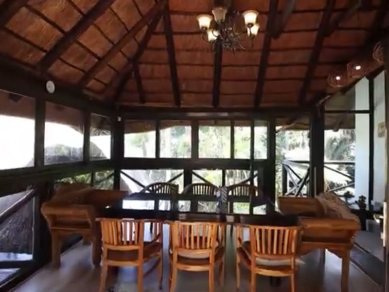 A covered patio area featuring a traditional thatched roof with exposed timber beams and extensive glass paneling, creating a bright and airy outdoor living space.