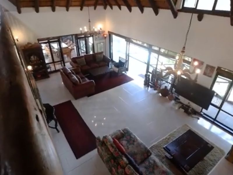 Spacious double-volume living area featuring exposed timber rafters, a thatched ceiling, and large glass sliding doors providing ample natural light.