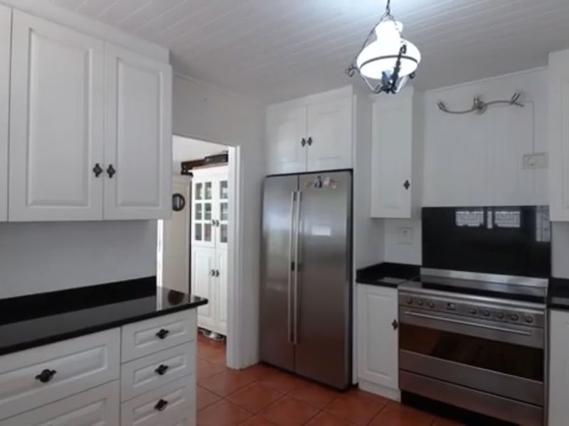 A well-maintained kitchen featuring white cabinetry, black granite countertops, stainless steel appliances, and terracotta floor tiles.