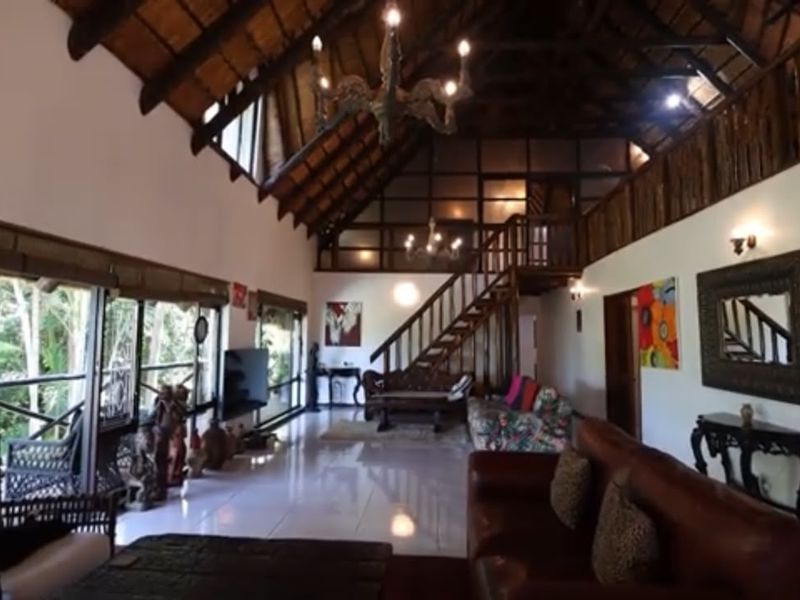 Spacious living area featuring a high thatched ceiling with exposed timber rafters, a mezzanine level, and large sliding doors opening to a balcony.