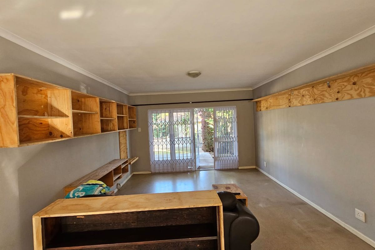 Living room featuring built-in plywood shelving units, carpeted flooring, and a security gate leading to an outdoor area.