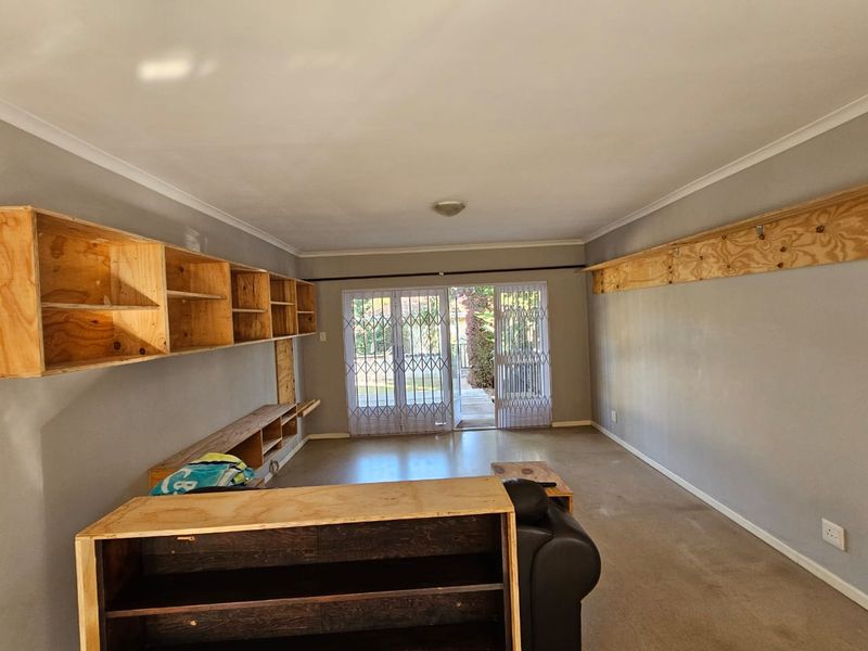 Living room featuring built-in plywood shelving units, carpeted flooring, and a security gate leading to an outdoor area.