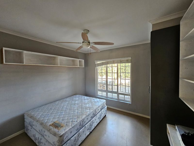 A functional bedroom featuring built-in shelving, a ceiling fan, and a built-in wardrobe, with natural light provided by a window with security bars.