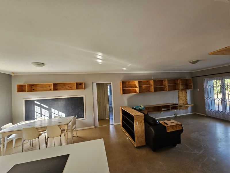Open-plan living and dining area featuring concrete floors, built-in wooden shelving units, a chalkboard wall, and access to an outdoor area via security gates.