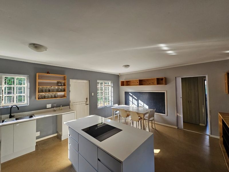 Spacious open-plan kitchen and dining area featuring a central island with induction hob, polished concrete floors, and ample natural light from multiple windows.