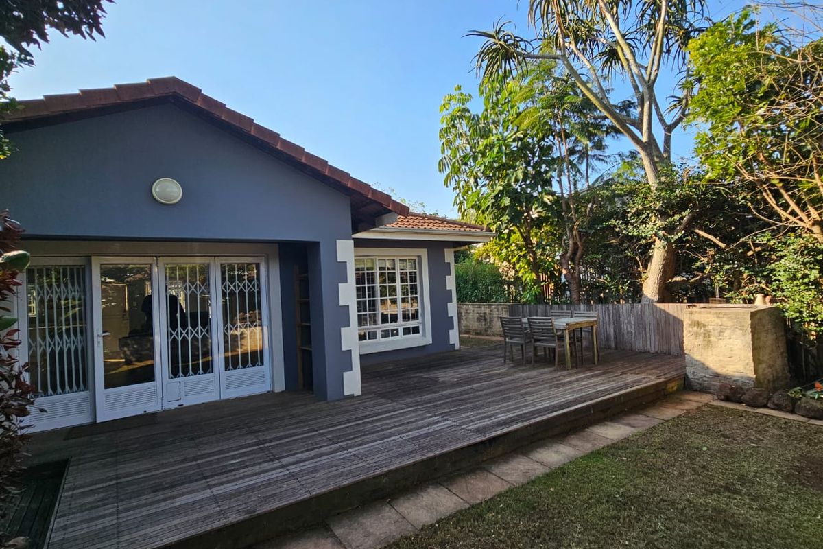 Rear view of the property featuring a spacious timber deck, security gates, and a well-established garden area.