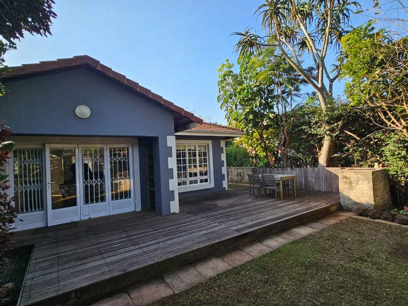 Rear view of the property featuring a spacious timber deck, security gates, and a well-established garden area.