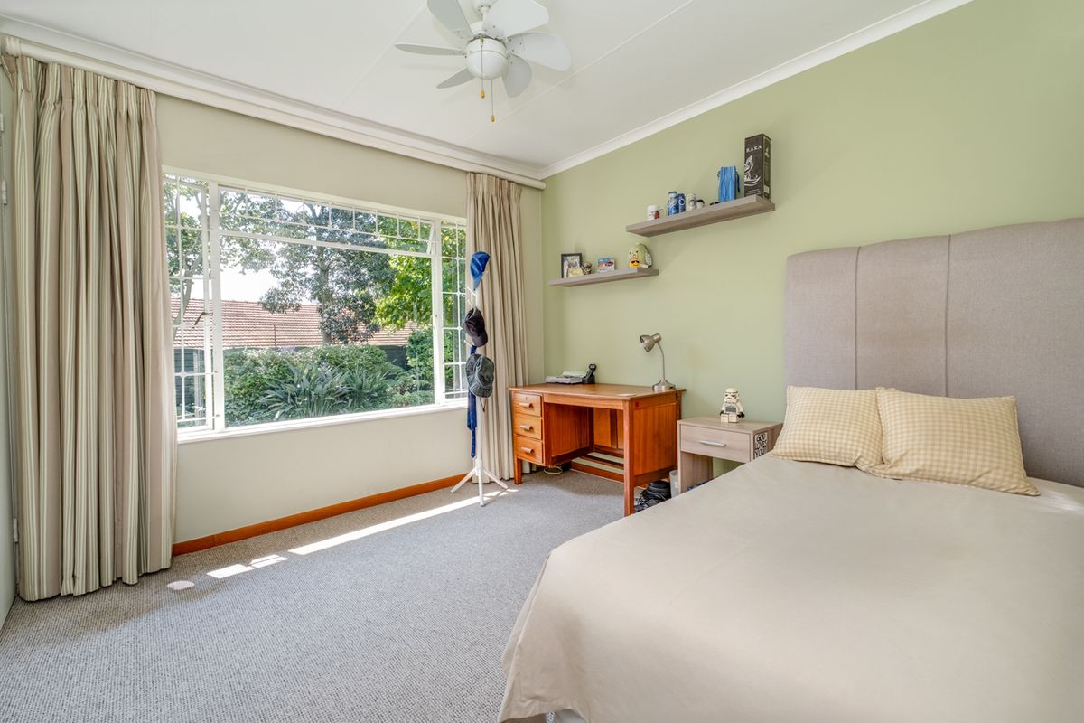 A well-lit bedroom featuring carpet flooring, a ceiling fan, and a large window with garden views.