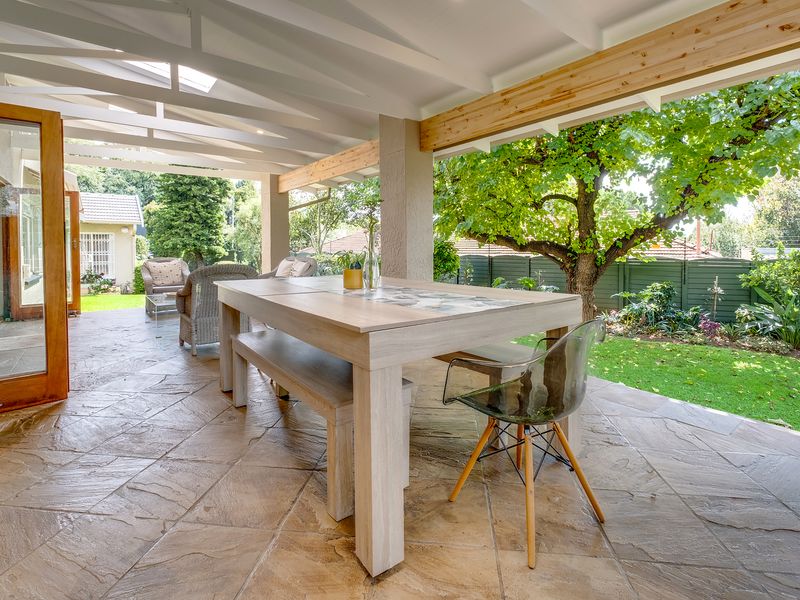 A spacious covered patio featuring flagstone flooring and exposed timber beams, providing a seamless transition to the landscaped garden area.