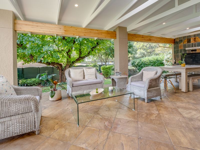 Spacious covered patio featuring stone tile flooring, exposed timber beams, and a built-in fireplace with slate surround, overlooking the garden.