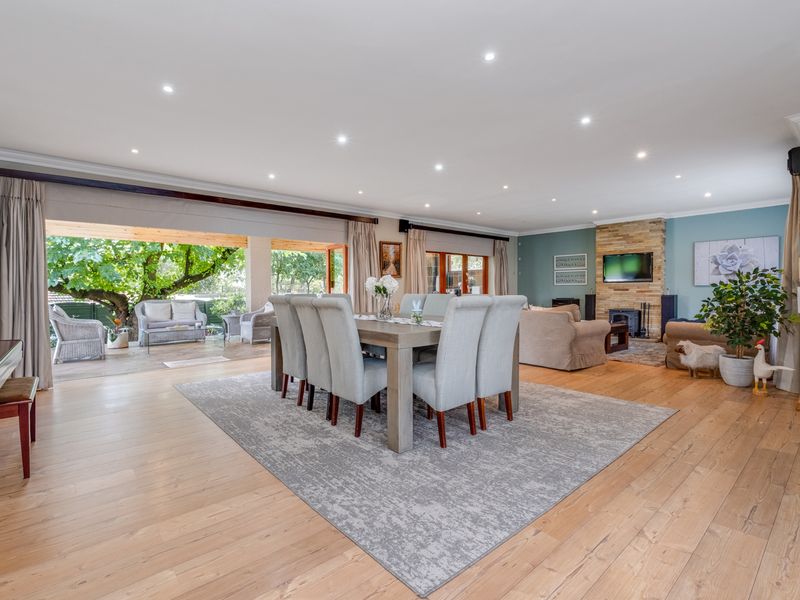 Spacious open-plan living and dining area featuring timber flooring, recessed lighting, and a stone-clad fireplace, with seamless flow to a covered outdoor patio.