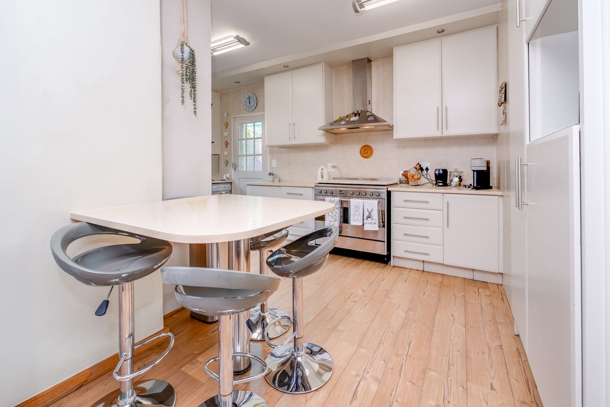 A functional kitchen featuring white cabinetry, stainless steel appliances, a tiled backsplash, and light-toned laminate flooring with an integrated breakfast nook area.