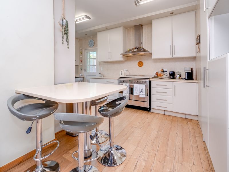 A functional kitchen featuring white cabinetry, stainless steel appliances, a tiled backsplash, and light-toned laminate flooring with an integrated breakfast nook area.