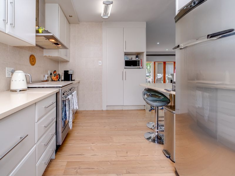 A well-maintained kitchen featuring light-toned cabinetry, stone countertops, a stainless steel gas stove, and a breakfast bar, with durable laminate flooring throughout.