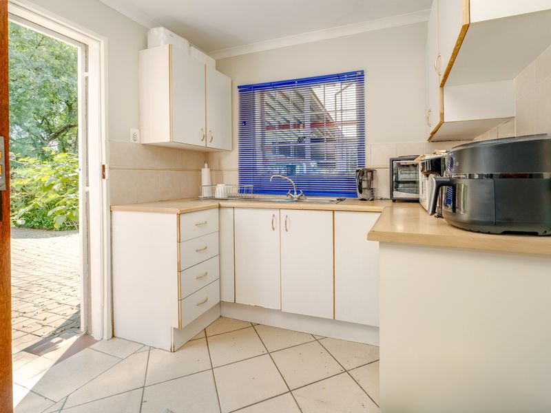 A functional scullery area featuring built-in white cabinetry, laminate countertops, a stainless steel sink, and direct access to the outdoor patio.