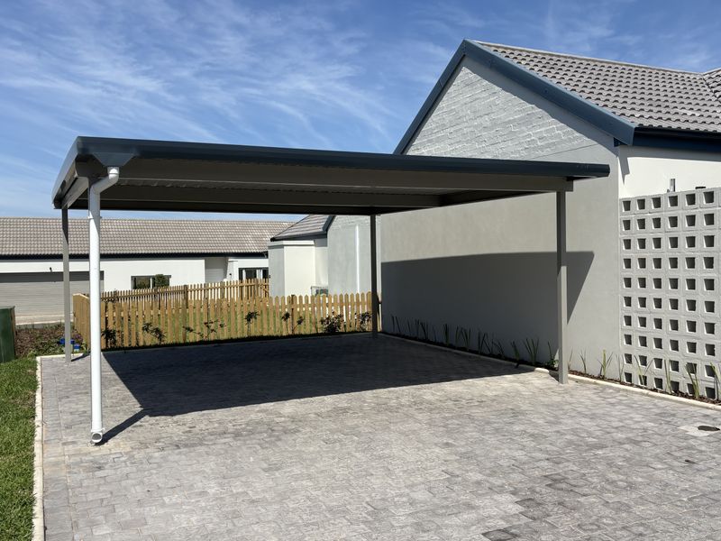 A modern, well-maintained double carport with a paved driveway and decorative concrete block screen wall, providing covered parking space.