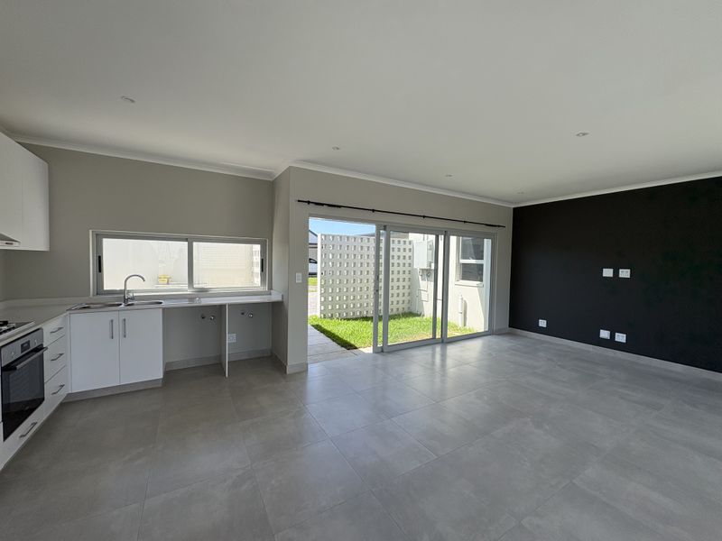 Modern open-plan living area featuring a sleek kitchen with built-in appliances, large format floor tiles, and sliding doors leading to a private garden.
