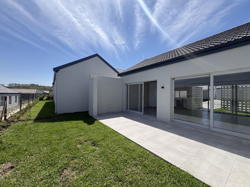 A well-maintained rear exterior view featuring a paved patio, large sliding glass doors, and a neat lawn area.