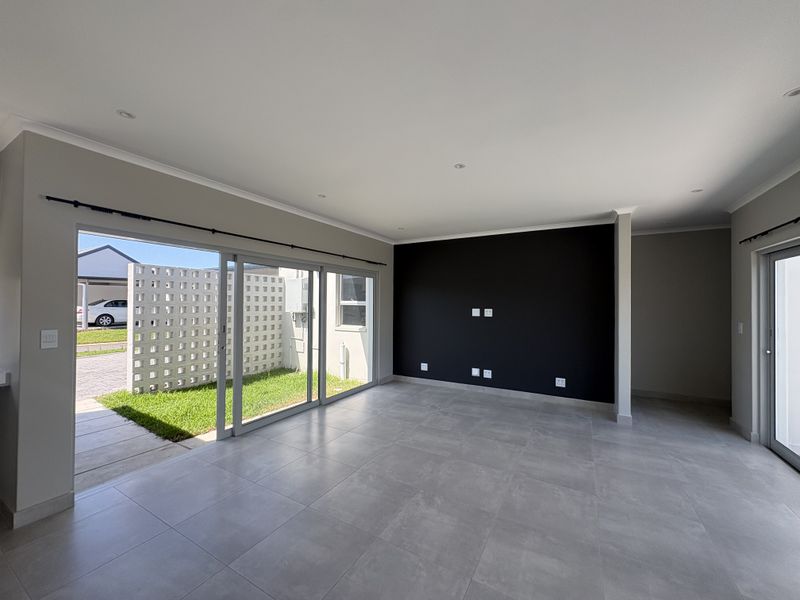 A bright, modern open-plan living area featuring large sliding glass doors, neutral tiled flooring, and a striking black accent wall.