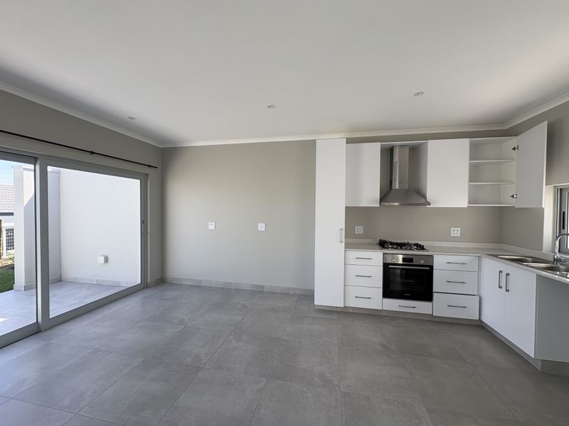 Modern open-plan kitchen and living area featuring sleek white cabinetry, built-in appliances, tiled floors, and large sliding doors leading to an outdoor patio.