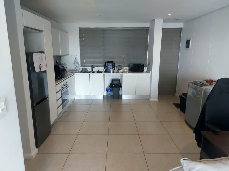 A functional kitchen featuring white cabinetry, tiled flooring, integrated oven and hob, and large windows with venetian blinds.