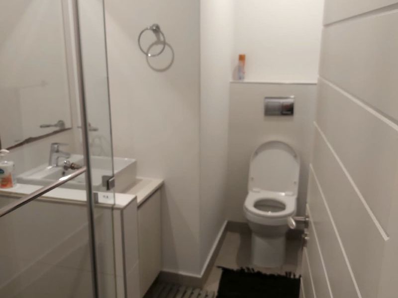 Modern bathroom featuring a wall-mounted toilet, glass shower enclosure, and a sleek vanity basin with chrome fixtures.