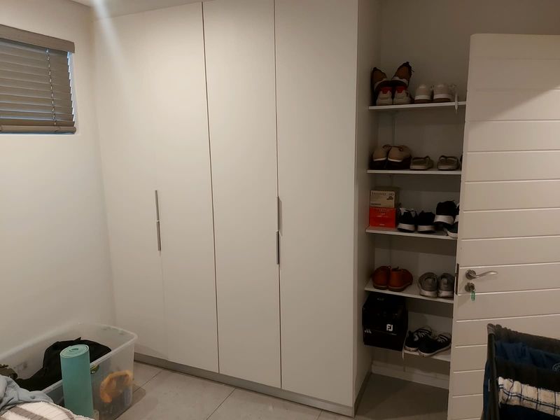 A bedroom featuring modern white built-in cupboards and integrated open shelving, complemented by tiled flooring and venetian blinds.
