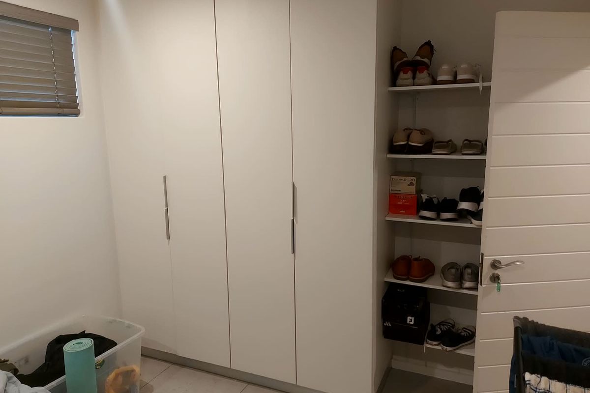 A bedroom featuring modern white built-in cupboards and integrated open shelving, complemented by tiled flooring and venetian blinds.