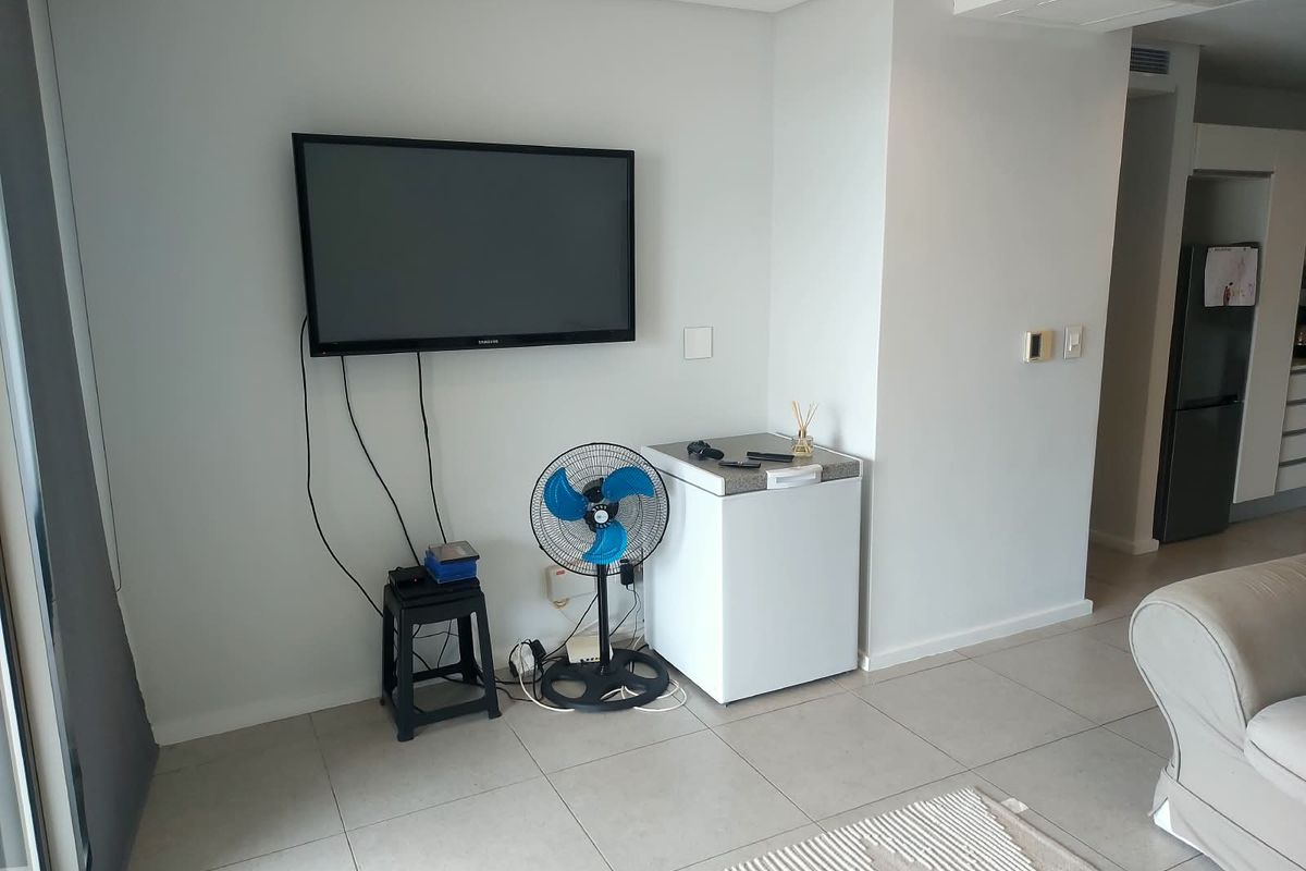 A living area featuring neutral tiled flooring and recessed ceiling lighting, with a wall-mounted television and visible electrical cabling.