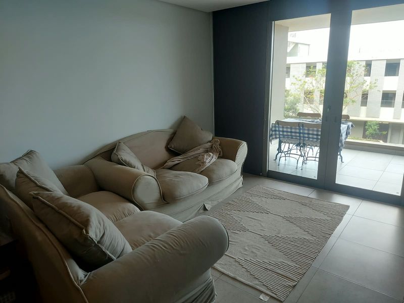 A bright living room featuring large sliding glass doors that open onto a private balcony, with neutral tiled flooring and modern finishes.