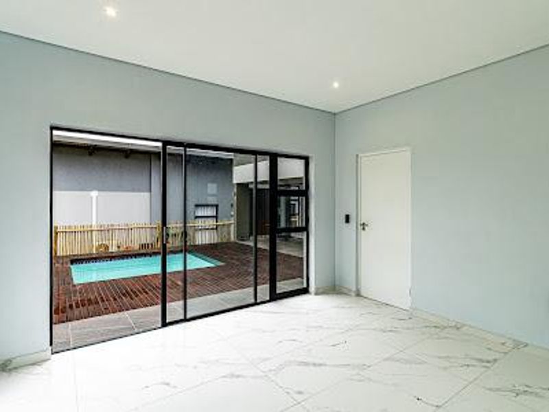 A bright, empty living area featuring large sliding glass doors that open onto a private patio and swimming pool area.