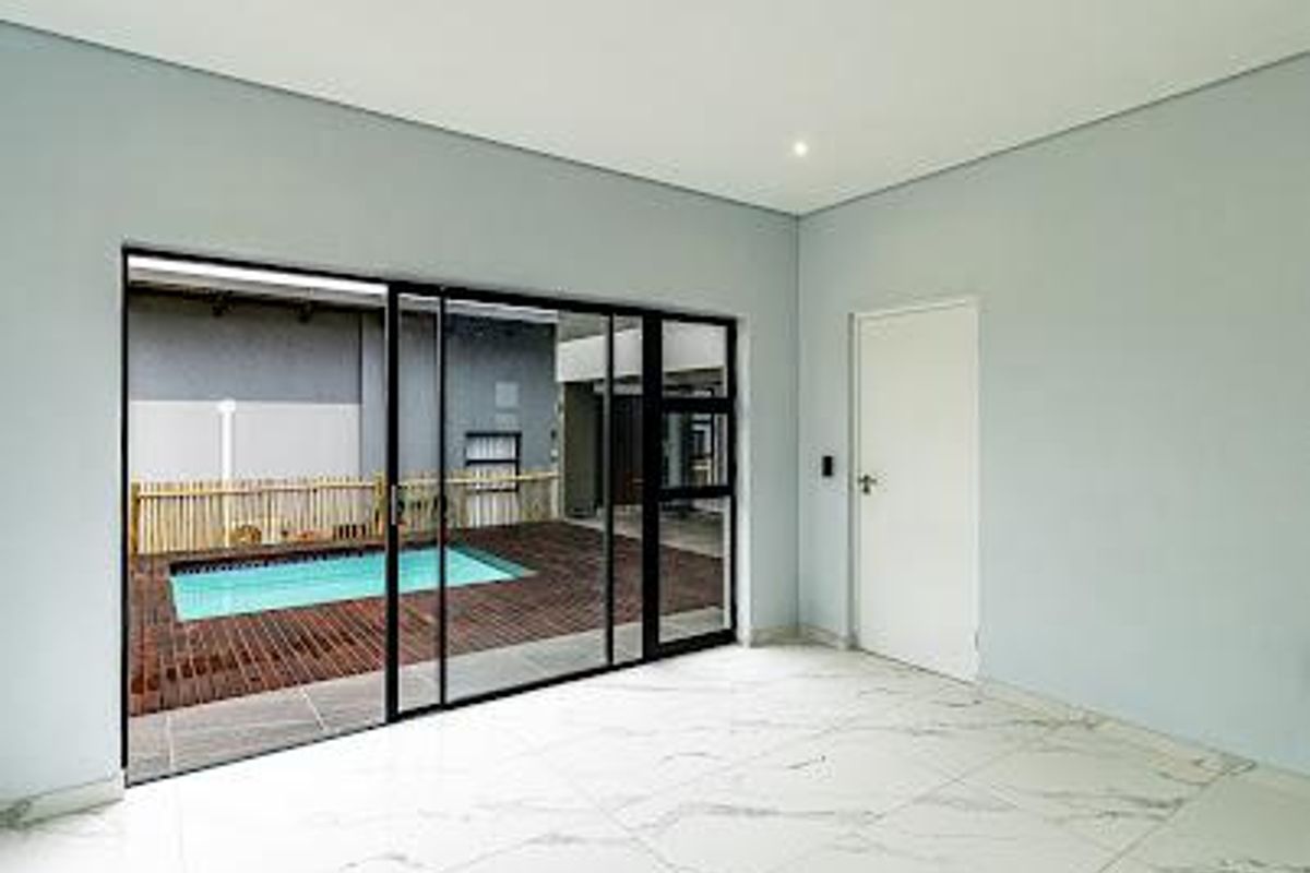 A bright, empty living area featuring large sliding glass doors that open onto a private patio and swimming pool area.