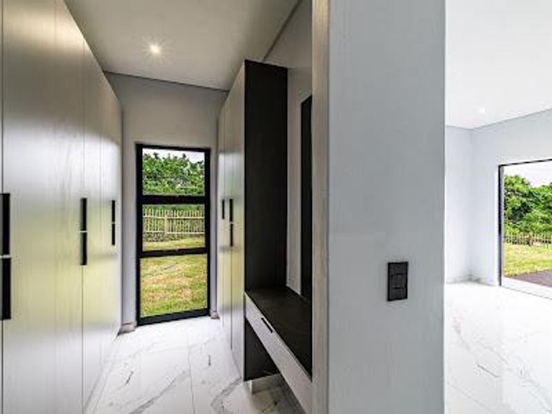 Modern bedroom featuring sleek built-in cupboards, a dedicated vanity area, and high-quality marble-look floor tiles with large windows overlooking the garden.
