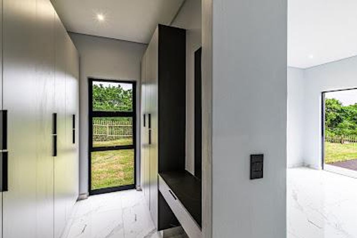 Modern bedroom featuring sleek built-in cupboards, a dedicated vanity area, and high-quality marble-look floor tiles with large windows overlooking the garden.