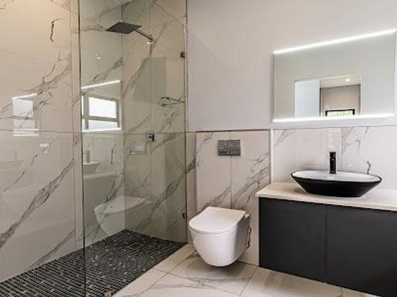 Modern bathroom featuring a walk-in shower with rain head, wall-hung toilet, vanity with vessel sink, and elegant marble-look wall tiling.