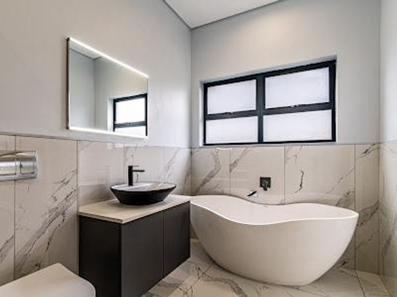 Modern bathroom featuring a sleek freestanding bathtub, vessel sink on a dark vanity, backlit mirror, and elegant marble-look tiling throughout.