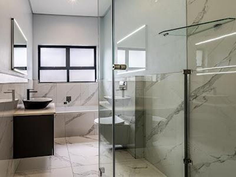 Modern bathroom featuring a floating vanity, vessel sink, glass-enclosed shower, built-in bathtub, and elegant marble-look tiling with integrated lighting.