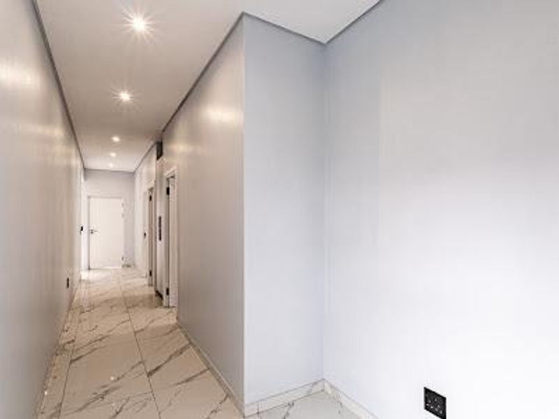 A bright, modern hallway featuring polished marble-look floor tiles and recessed downlighting, leading to multiple interior doorways.