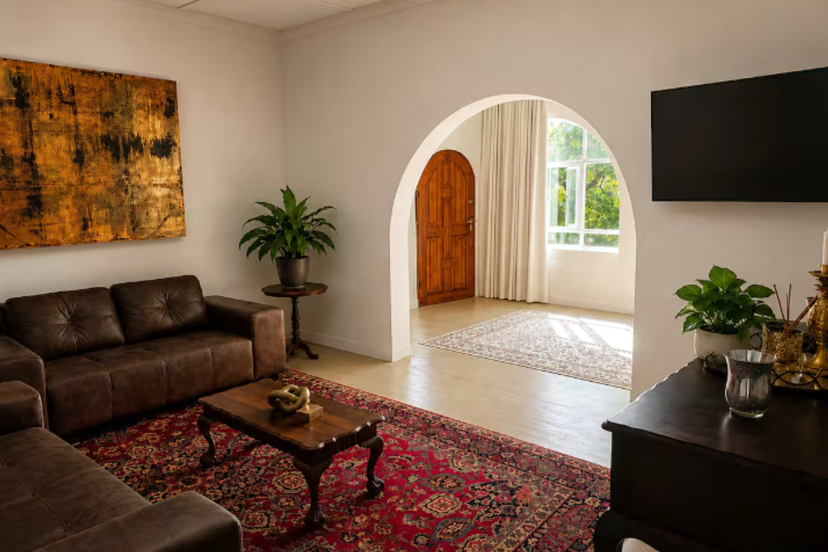A well-lit living room featuring a distinctive arched doorway leading to an entrance area with a solid timber door and natural light.