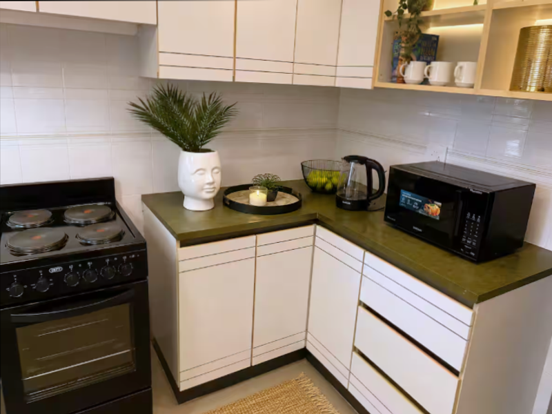 A compact kitchen featuring white cabinetry, a dark green countertop, tiled backsplash, and a freestanding electric stove with oven.